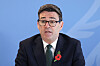 Andy Burnham taler foran en blå bakgrunn, iført mørk dress og rød valmue.