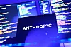 Anthropic-logo på en mørk skjerm foran skjermer med fargerik programkode.